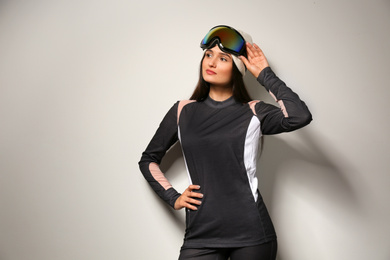 Woman wearing thermal underwear and goggles on light grey background. Winter sport clothes