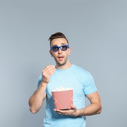Emotional man with 3D glasses and popcorn during cinema show on grey background