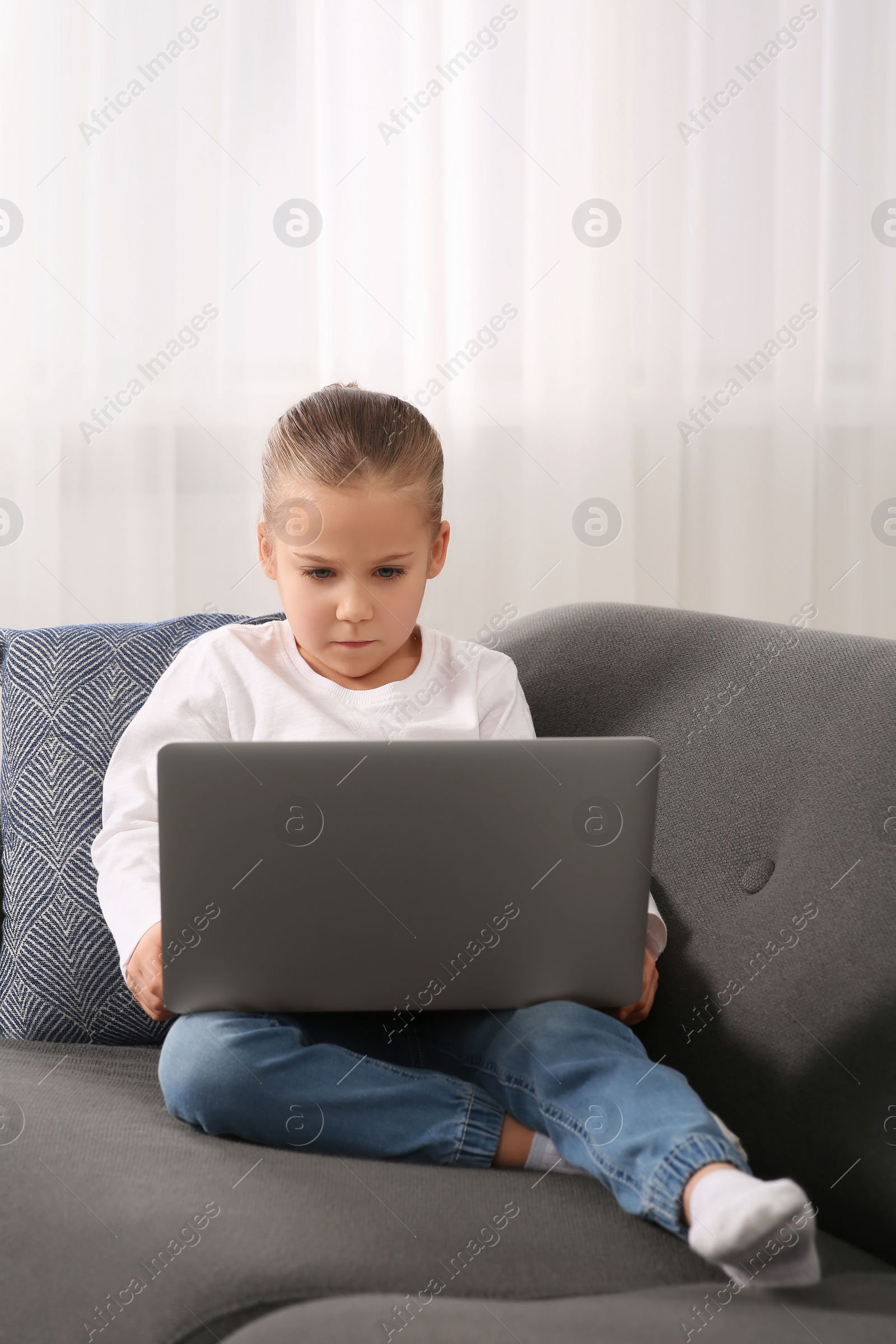 Photo of Little girl using laptop on sofa at home. Internet addiction