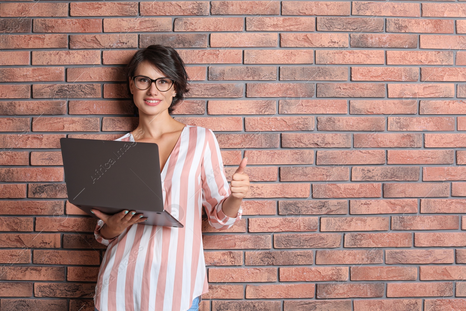 Photo of Young woman with modern laptop on brick wall background