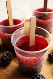 Photo of Tasty blackberry ice pops in plastic cups on table, closeup. Fruit popsicle