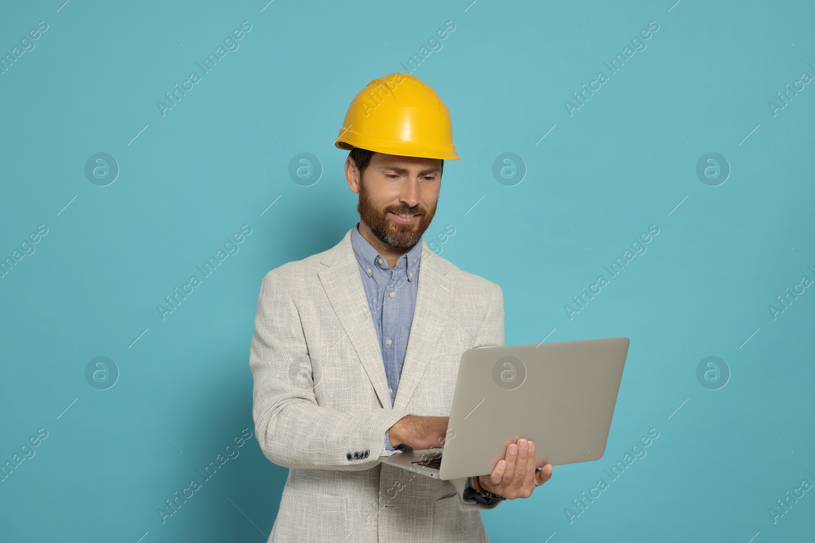 Photo of Professional engineer in hard hat with laptop on light blue background