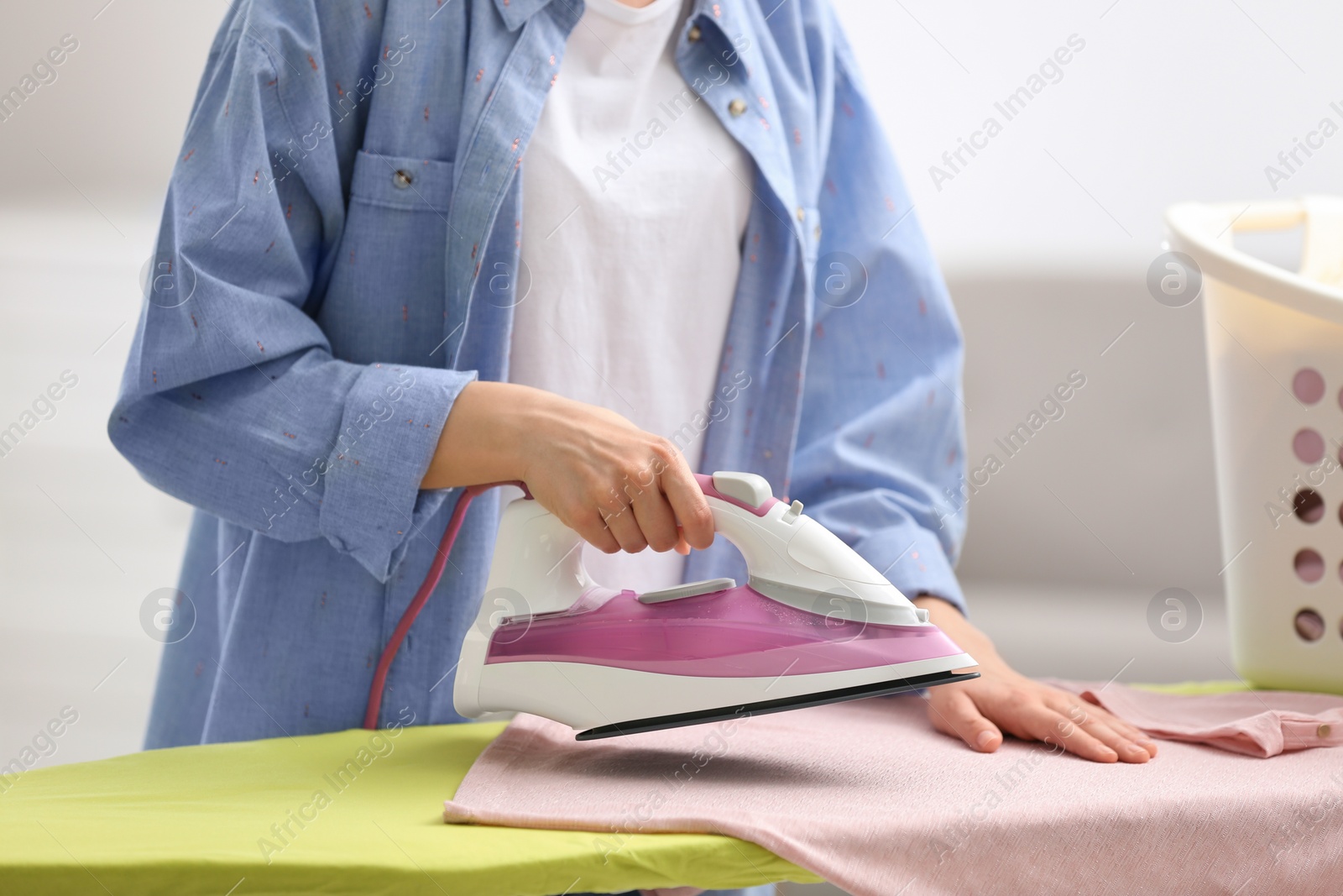 Photo of Young woman ironing clean laundry on board indoors, closeup