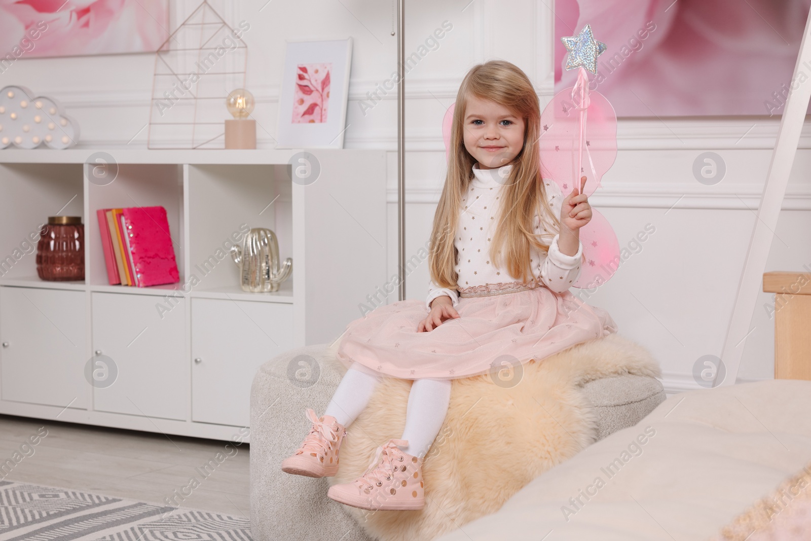 Photo of Cute little girl in fairy costume with pink wings and magic wand at home, space for text