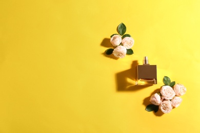 Photo of Flat lay composition with bottle of perfume and roses on color background, space for text