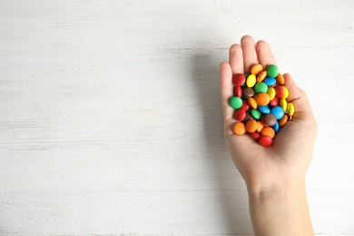 Photo of Woman holding glazed candies on white wooden background, top view. Space for text