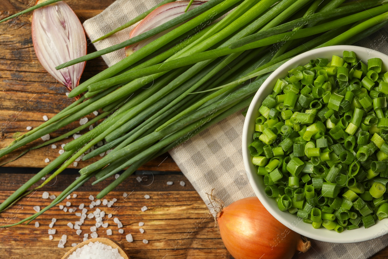 Photo of Chopped green onion in bowl on wooden table, flat lay