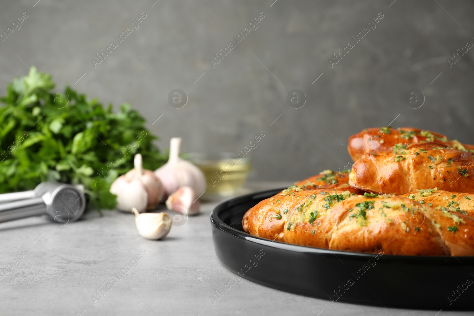 Photo of Plate of bread loaves with garlic and herbs on light table against grey background. Space for text