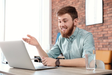 Photo of Young man using video chat on laptop in home office