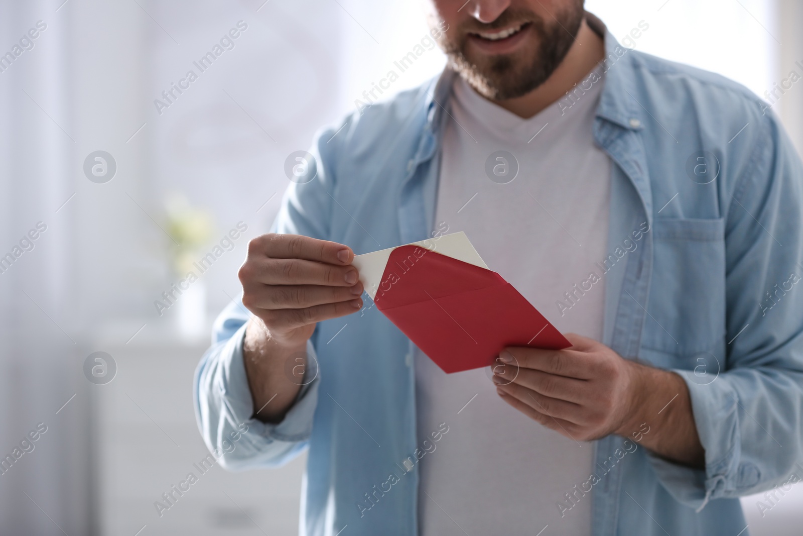 Photo of Man holding envelope with greeting card at home, closeup