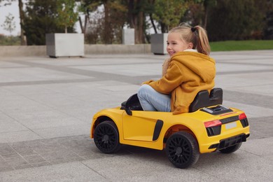 Cute little girl driving children's car on city street. Space for text