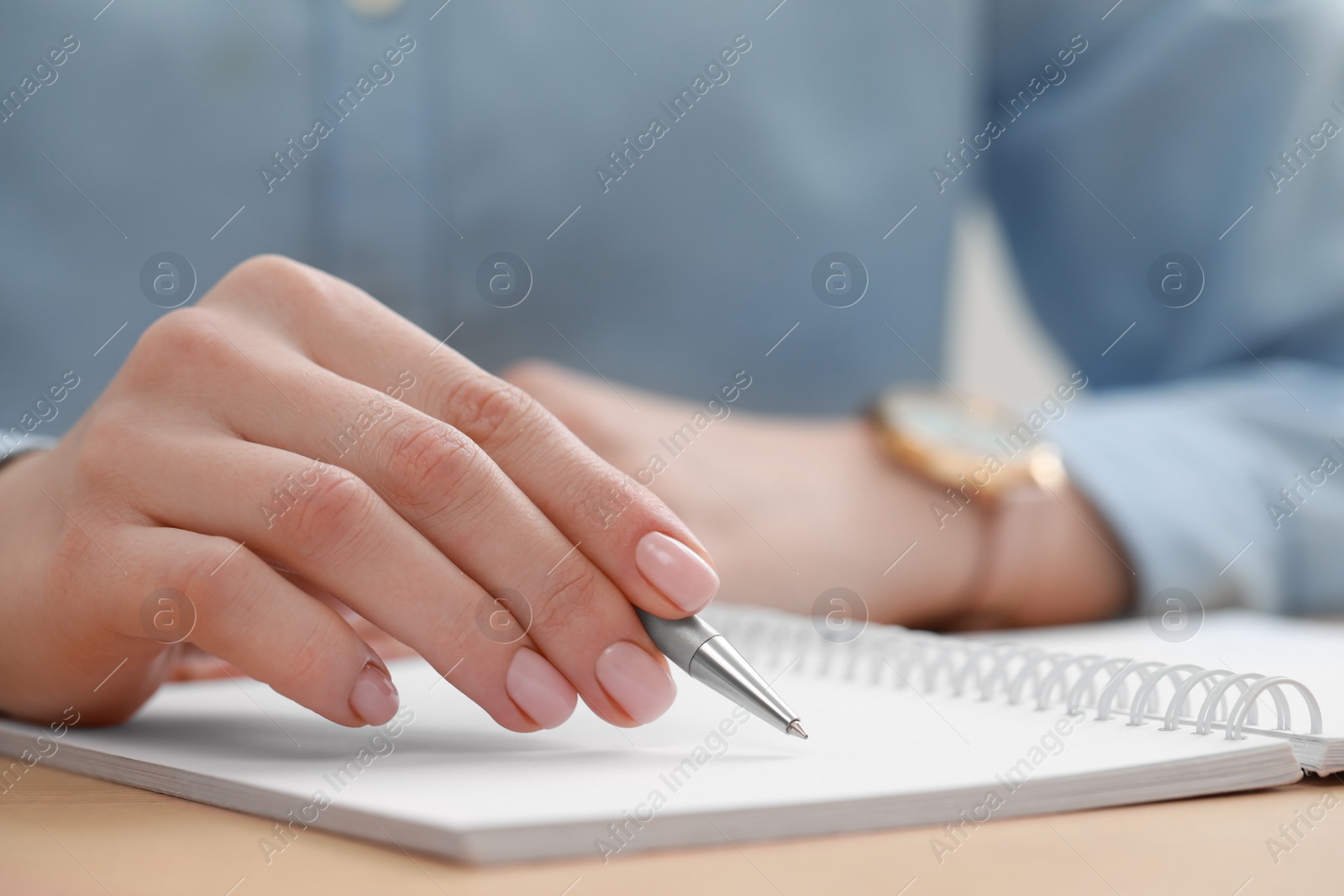 Photo of Woman writing in notebook at wooden table, closeup