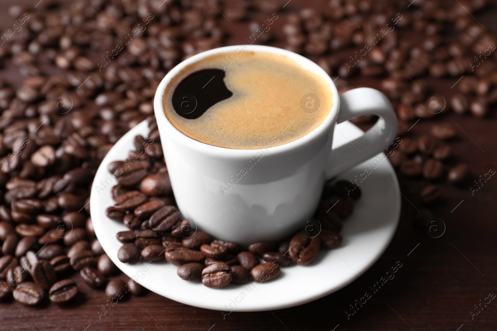 Photo of Cup of hot aromatic coffee and roasted beans on wooden table, closeup