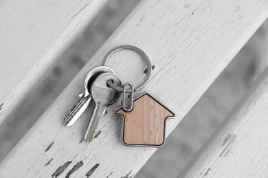 Keys with trinket in shape of house on wooden surface, top view. Real estate agent services