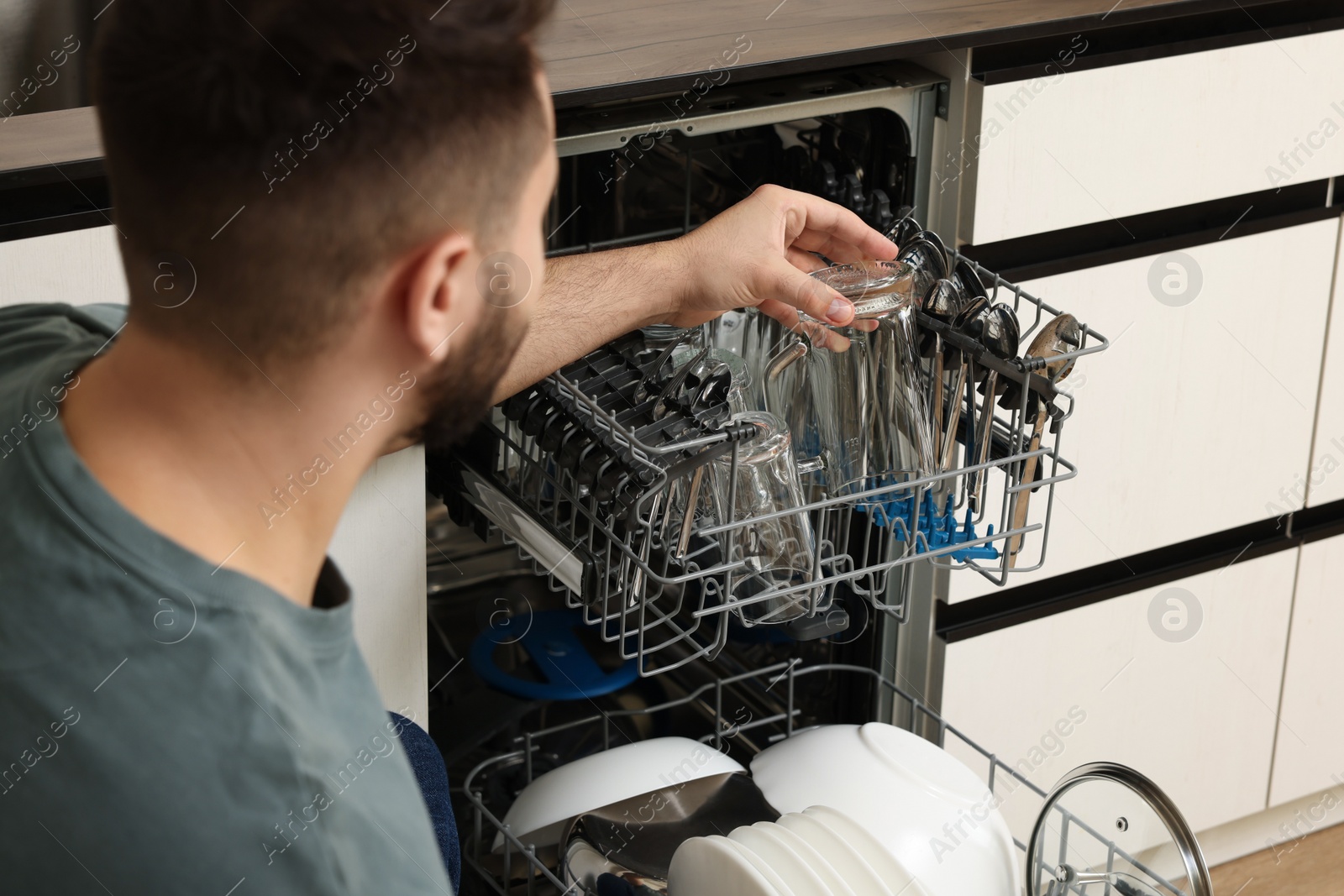 Photo of Man loading dishwasher with glasses in kitchen, closeup