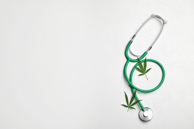 Photo of Stethoscope and hemp leaves on white background, flat lay. Space for text