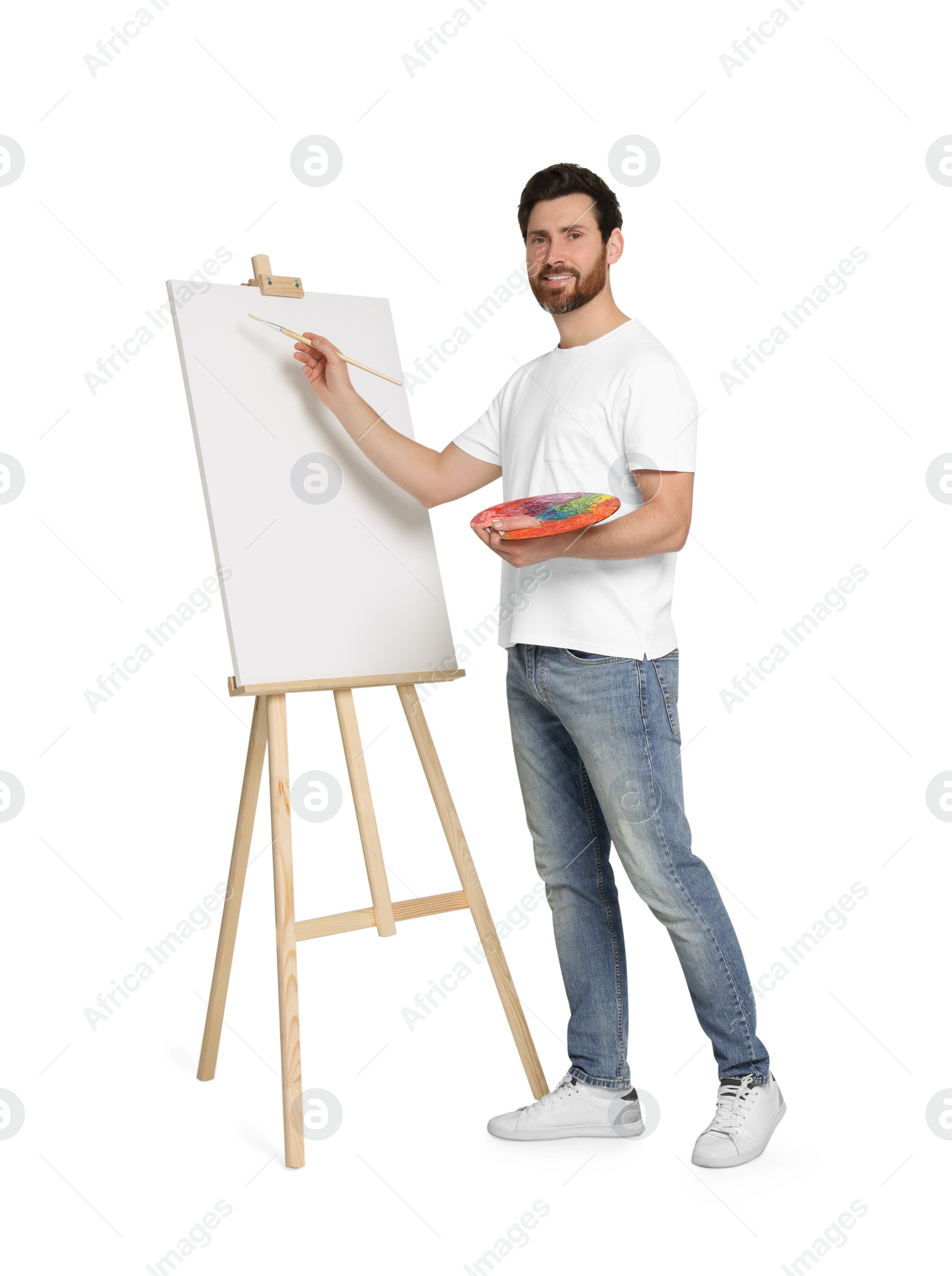 Photo of Man with brush painting against white background. Using easel to hold canvas