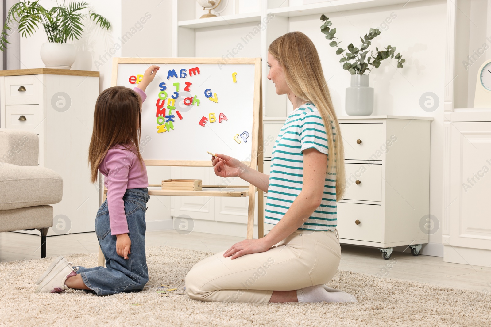 Photo of Mom teaching her daughter alphabet with magnetic letters at home