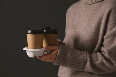 Photo of Woman holding takeaway cardboard cups on black background, closeup. Coffee to go