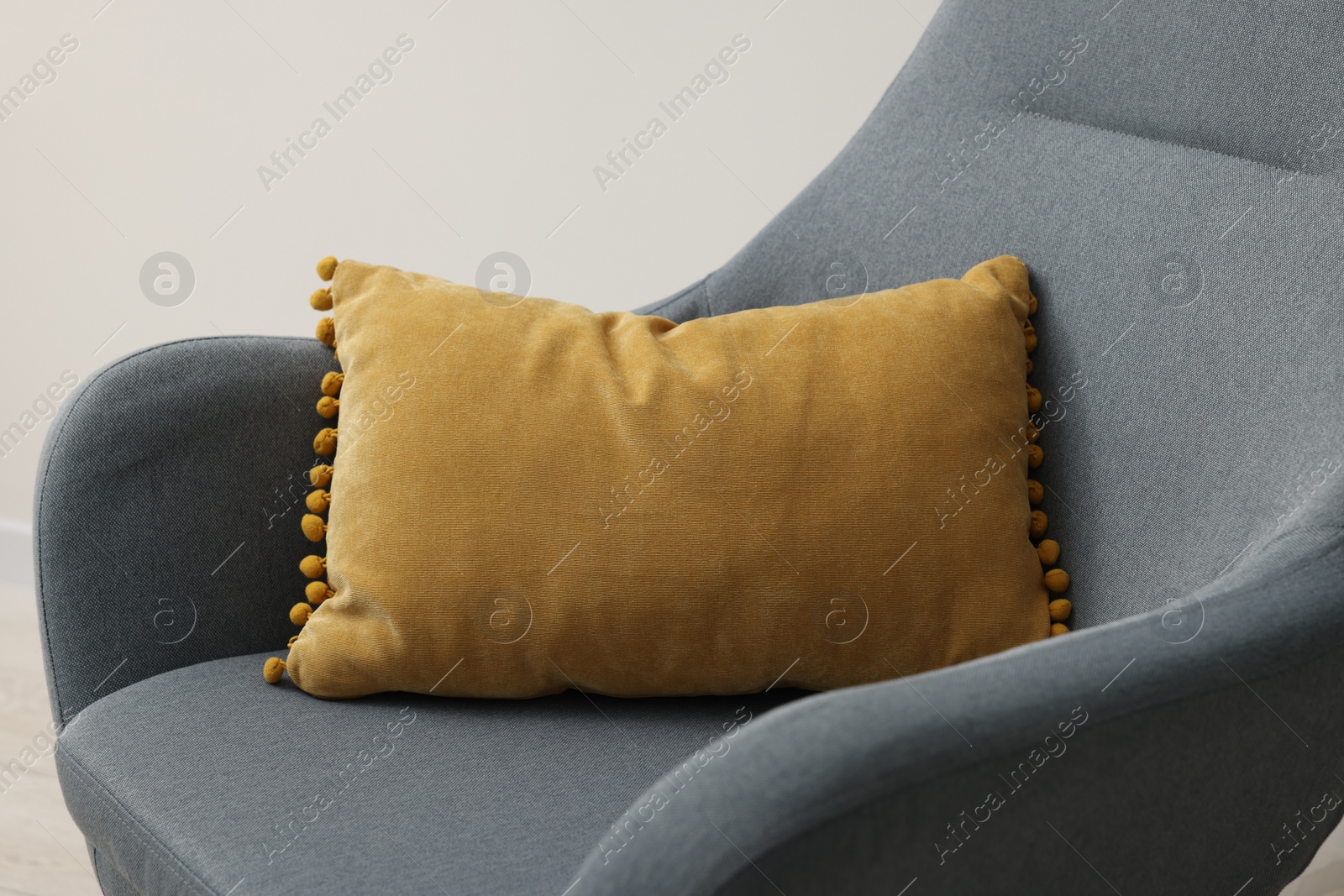 Photo of Soft pillow on armchair near light grey wall