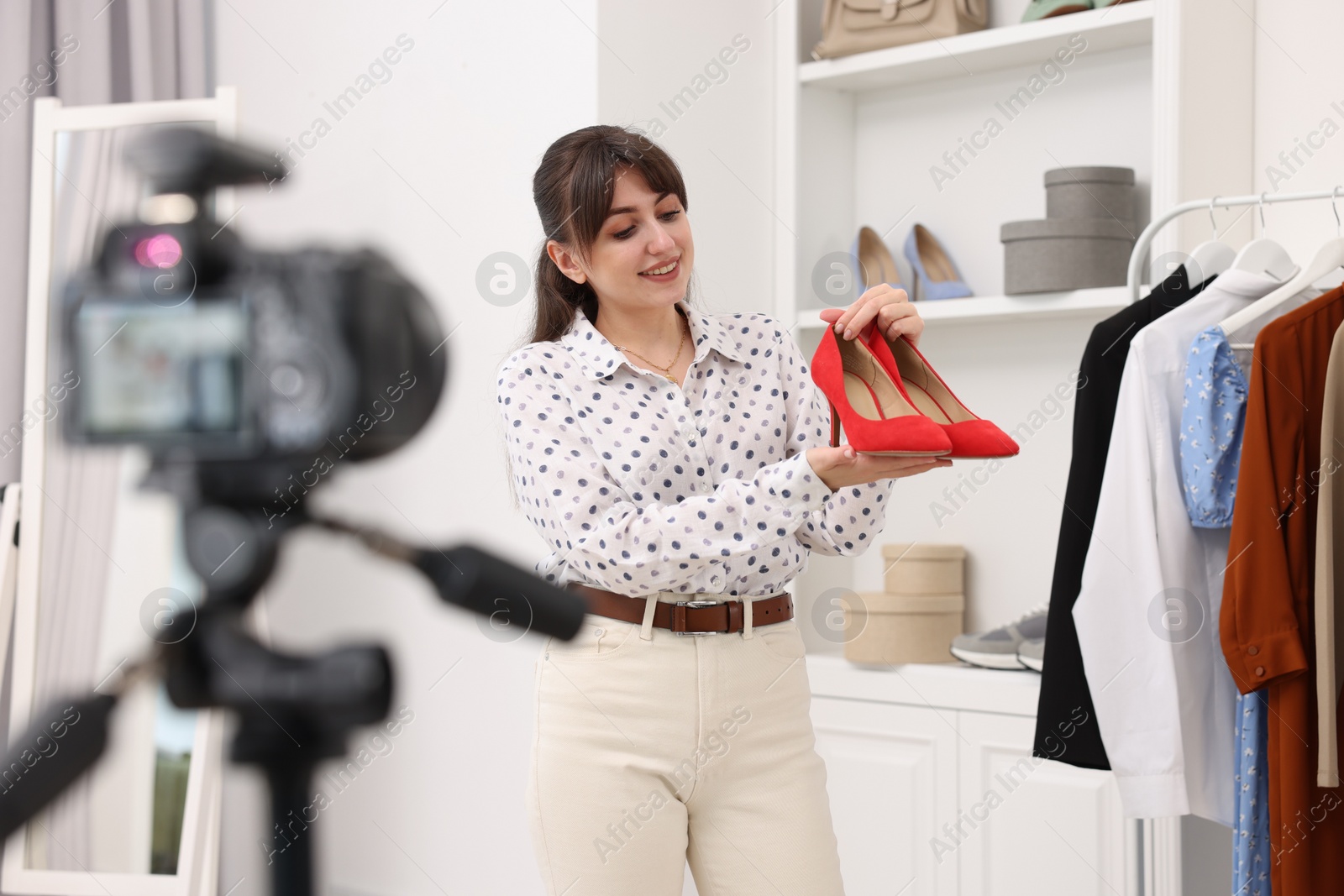 Photo of Smiling fashion blogger showing her shoes while recording video at home