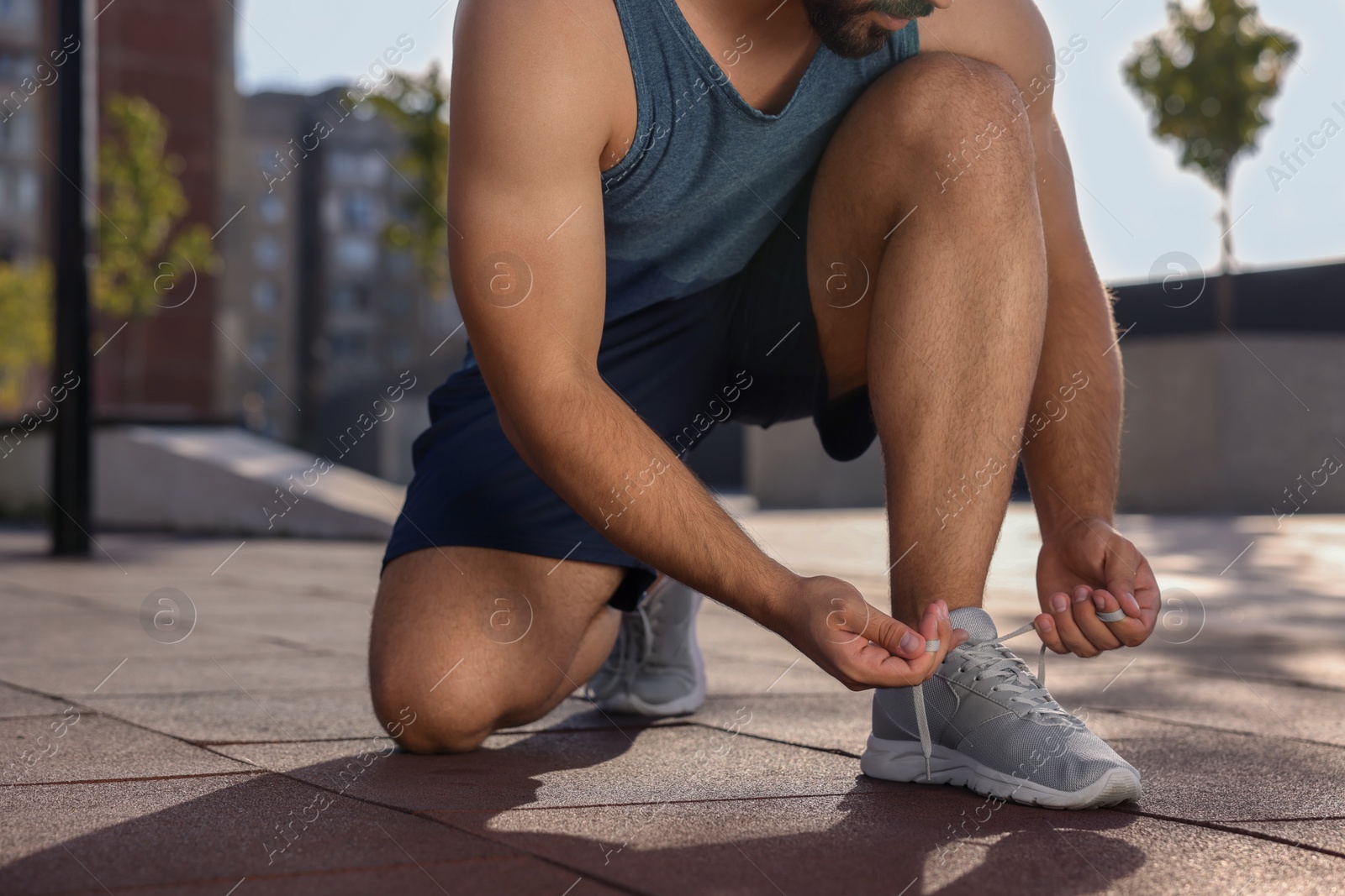 Photo of Man tying shoelaces before running outdoors on sunny day, closeup