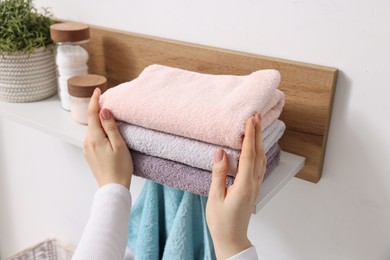 Photo of Woman stacking clean towels on shelf indoors, closeup