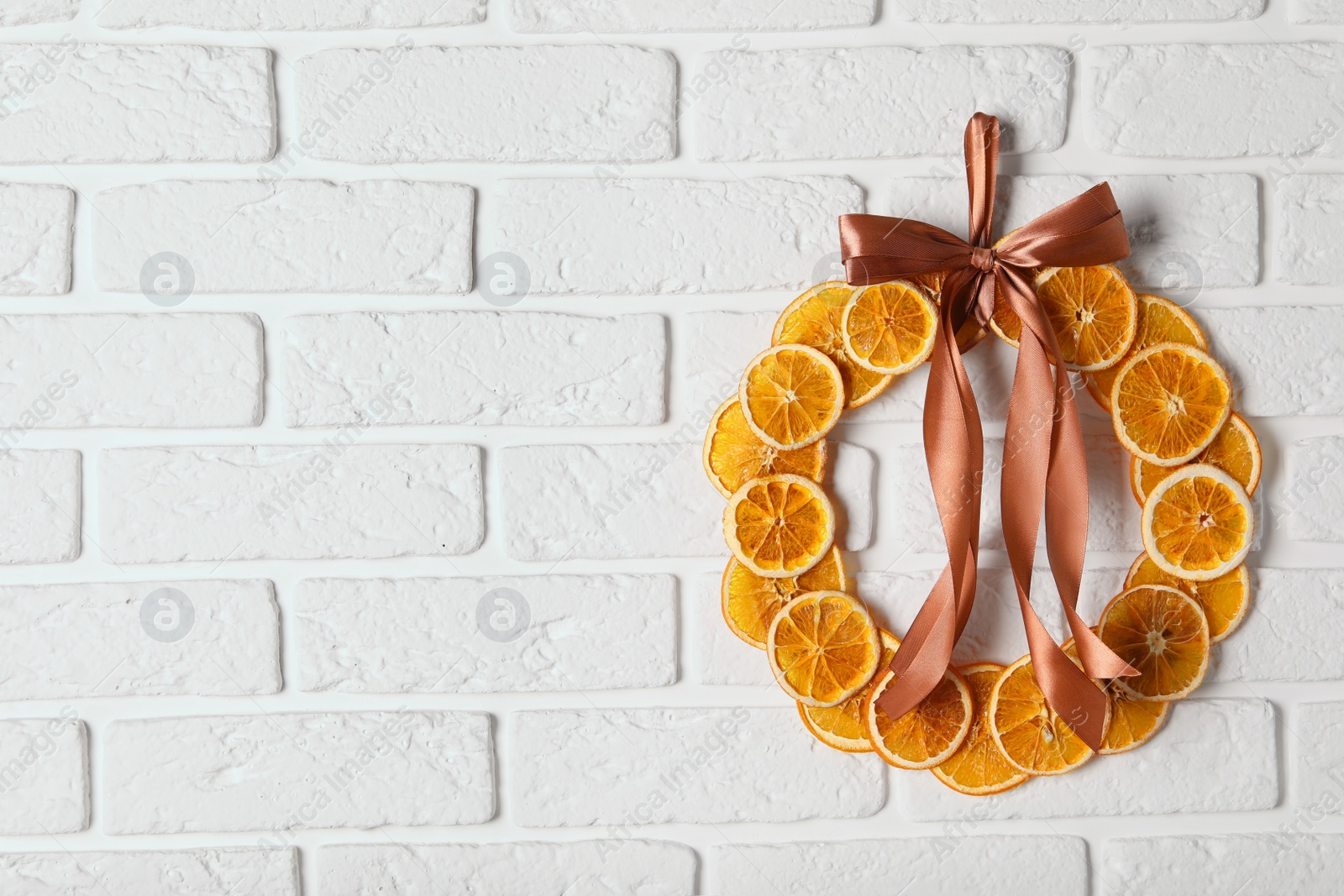 Photo of Decorative wreath made with dry oranges and ribbon hanging on white brick wall, space for text