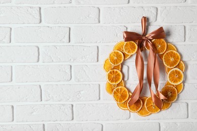 Photo of Decorative wreath made with dry oranges and ribbon hanging on white brick wall, space for text