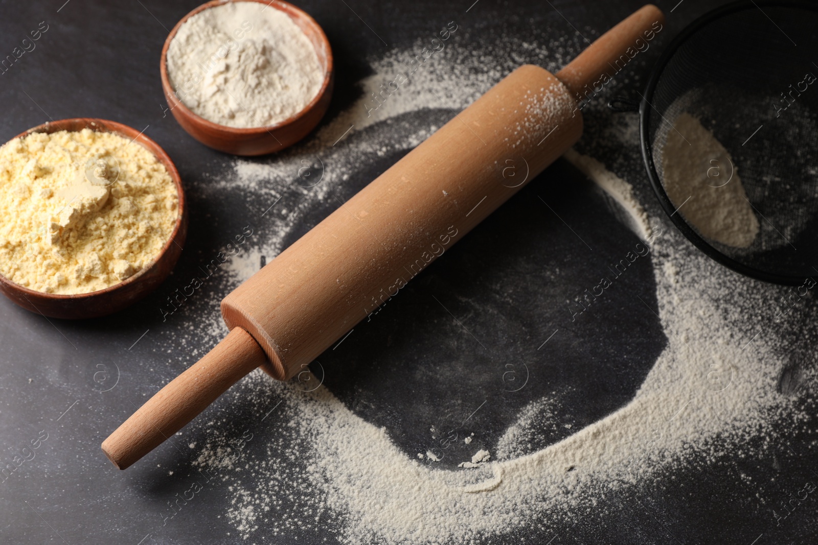 Photo of Scattered flour, rolling pin and sieve on black table