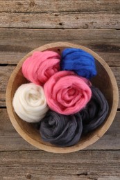 Photo of Colorful felting wool in bowl on wooden table, top view