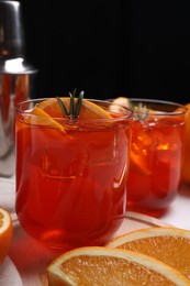 Aperol spritz cocktail, ice cubes, rosemary and orange slices in glasses on table, closeup