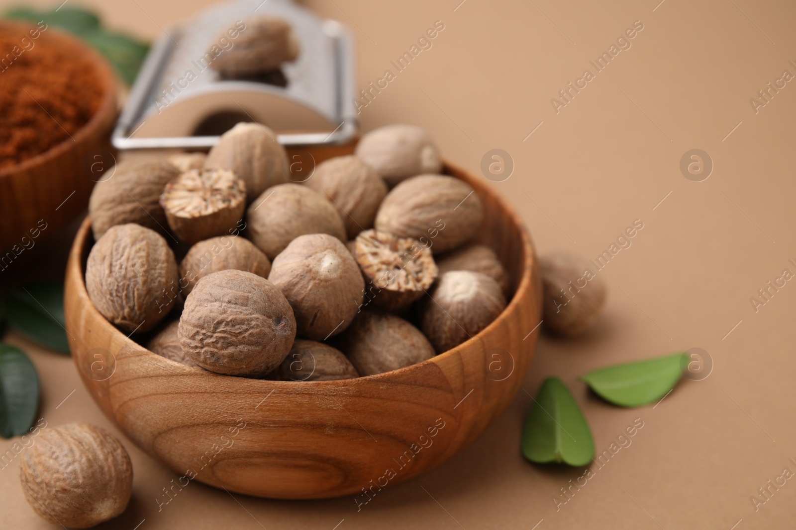 Photo of Nutmegs in bowl on light brown background, closeup. Space for text