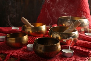 Photo of Tibetan singing bowls with mallets, candles and red fabric on wooden table