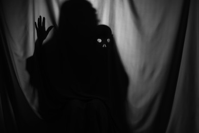 Silhouette of creepy ghost with skull behind grey cloth