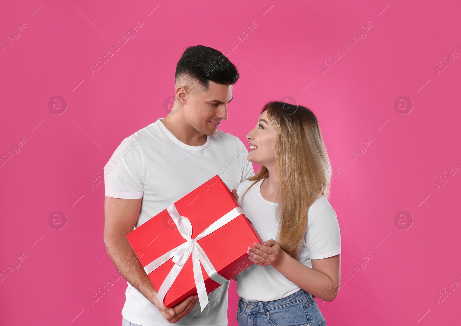 Photo of Man surprising his girlfriend with gift on pink background. Valentine's day celebration