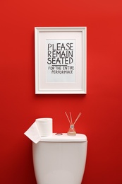 Photo of Toilet bowl and funny sign near red wall. Bathroom interior