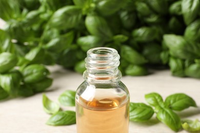 Photo of Glass bottle of basil essential oil and leaves on white table, closeup