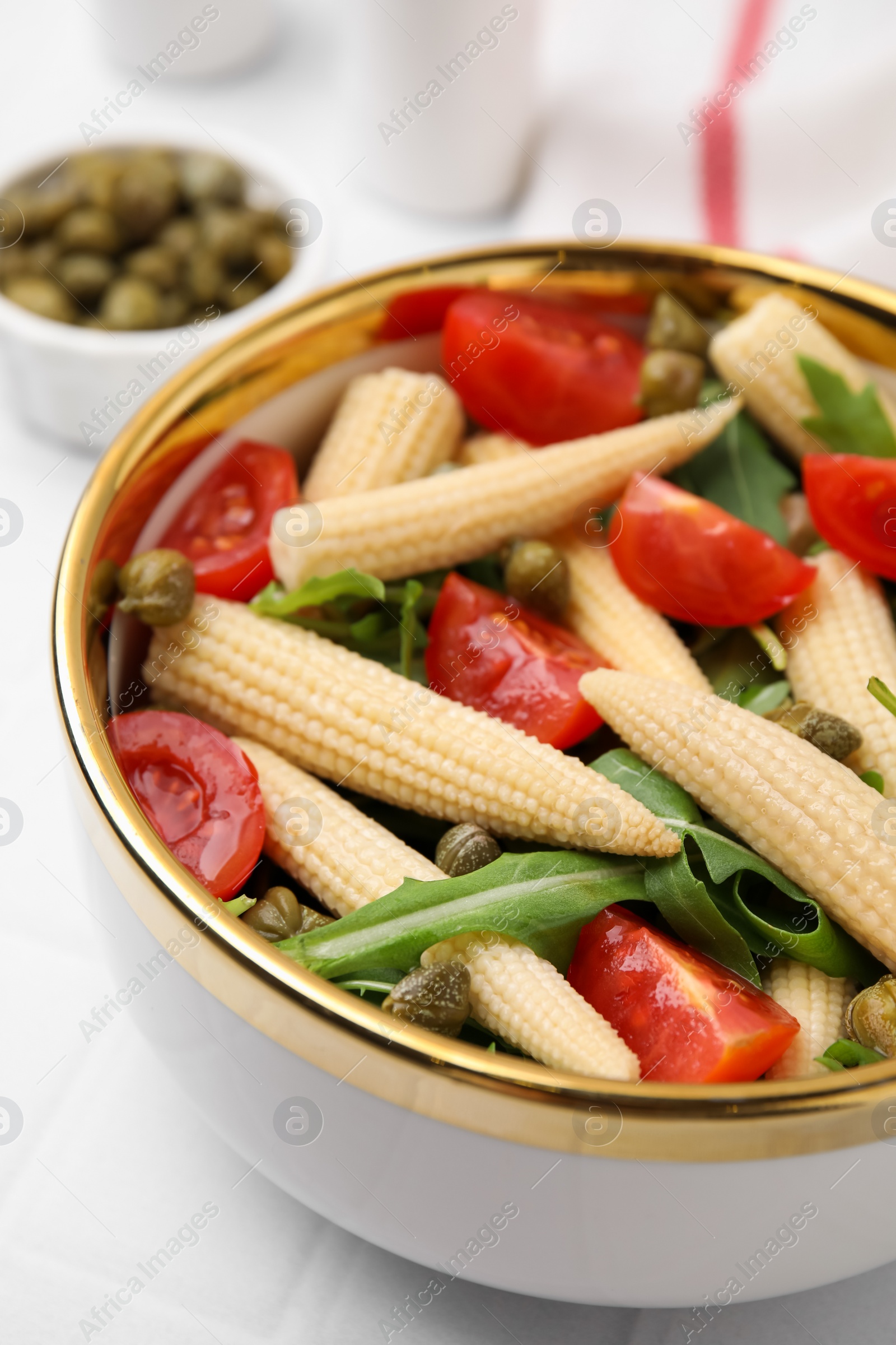 Photo of Tasty baby corn with tomatoes, arugula and capers on white tiled table, closeup