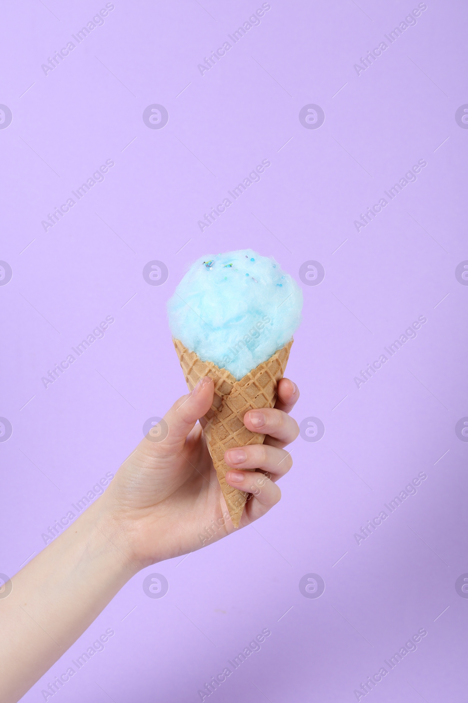 Photo of Woman holding waffle cone with cotton candy on violet background, closeup