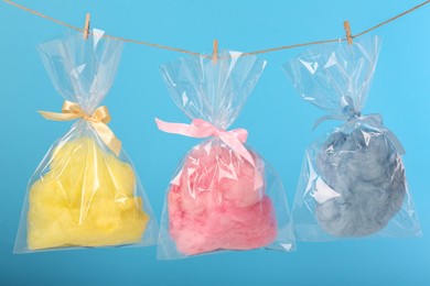 Photo of Packaged sweet cotton candies hanging on clothesline against light blue background