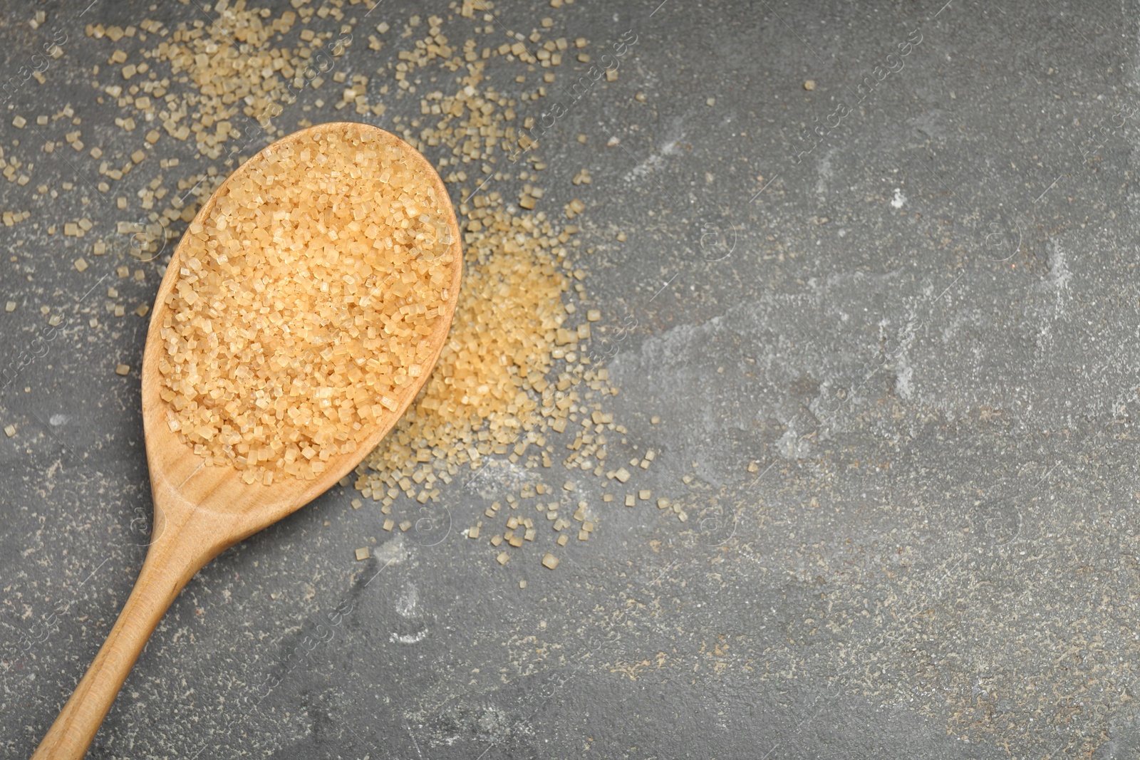 Photo of Spoon with brown sugar on grey textured table, top view. Space for text