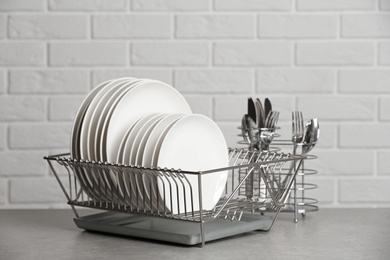 Photo of Dish rack with clean plates on table near brick wall