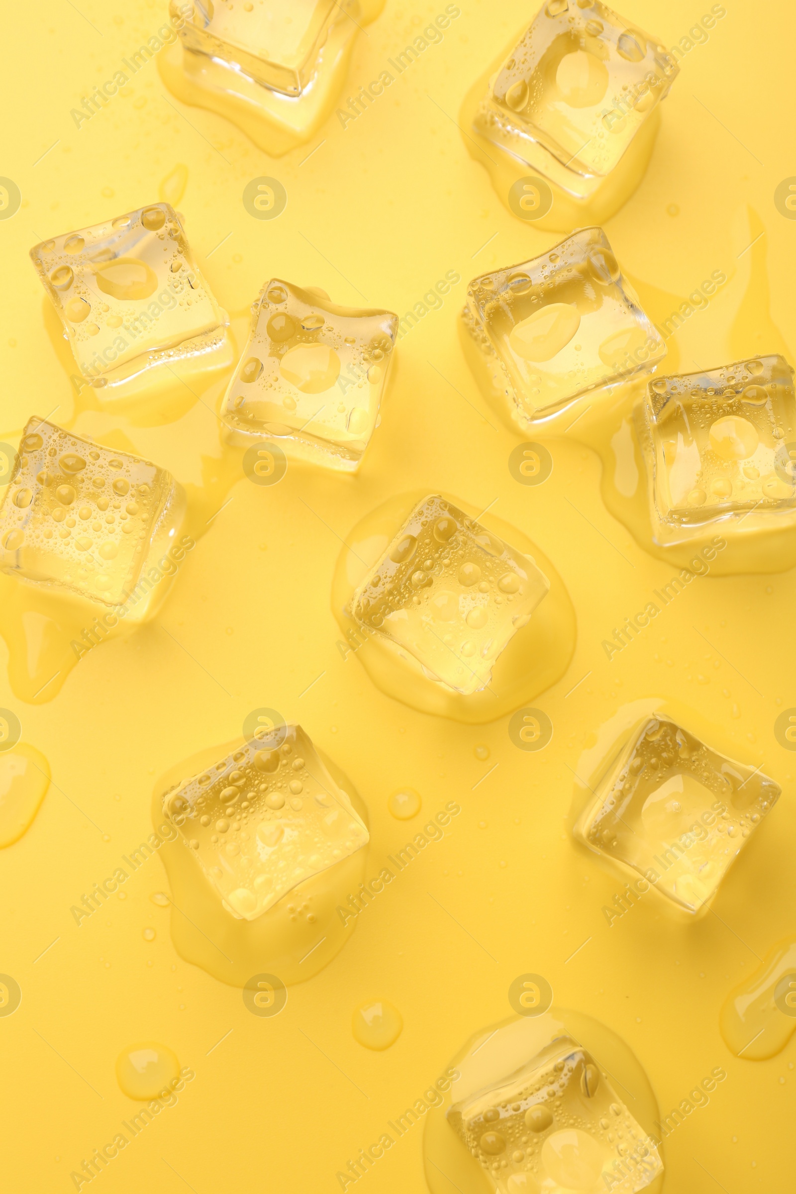 Photo of Crystal clear ice cubes on yellow background, flat lay