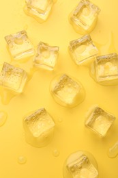 Photo of Crystal clear ice cubes on yellow background, flat lay