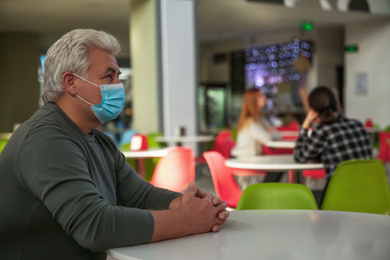 Photo of Senior man with medical mask in cafe. Virus protection