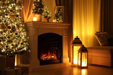 Photo of Beautiful fireplace, Christmas tree and other decorations in living room at night. Interior design