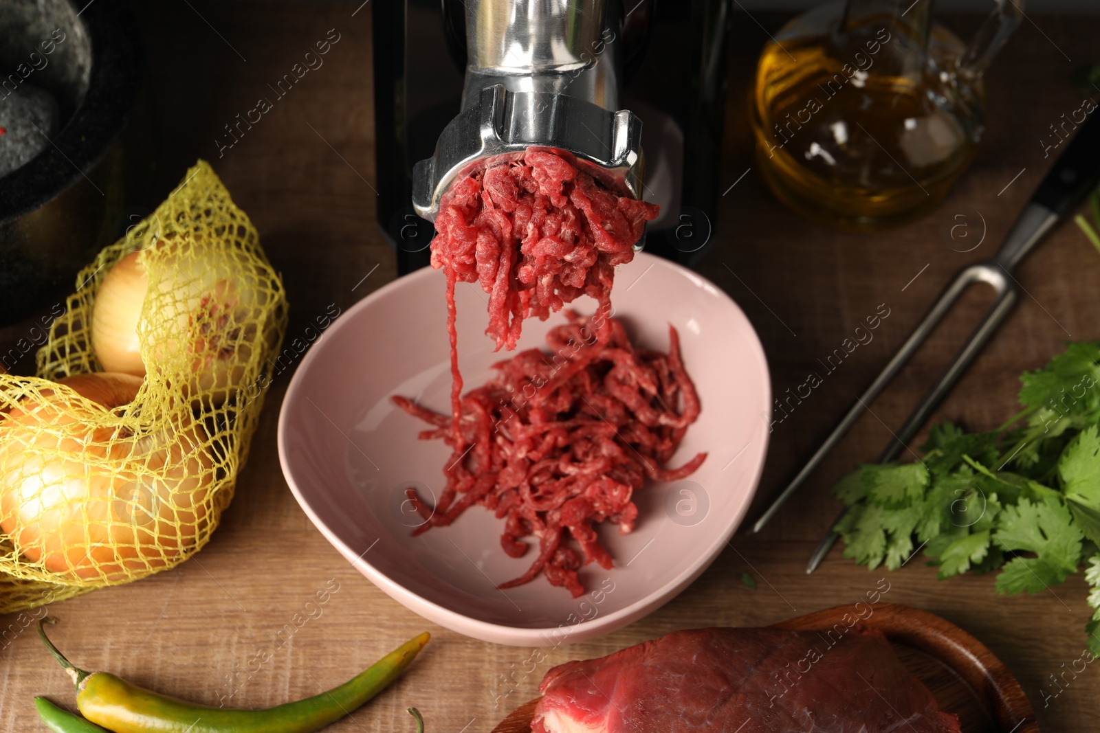 Photo of Mincing beef with electric meat grinder on wooden table, above view