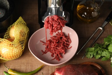 Photo of Mincing beef with electric meat grinder on wooden table, above view