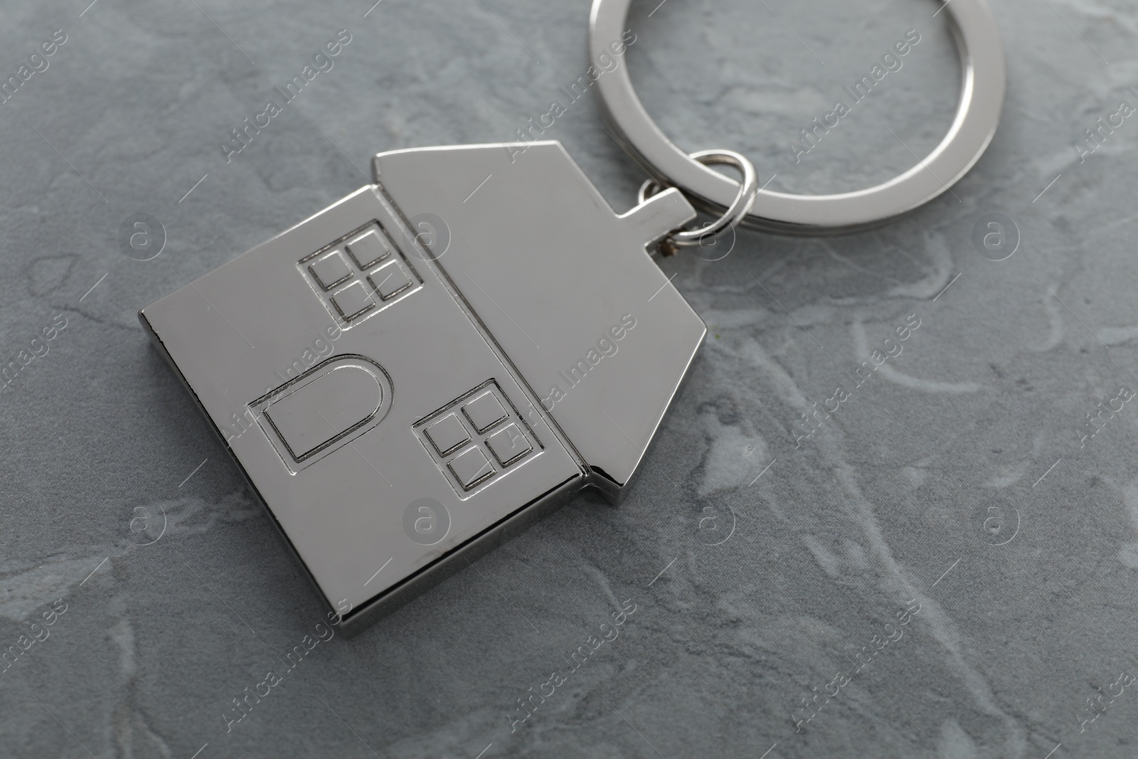 Photo of Metal keychain in shape of house on grey marble table, closeup